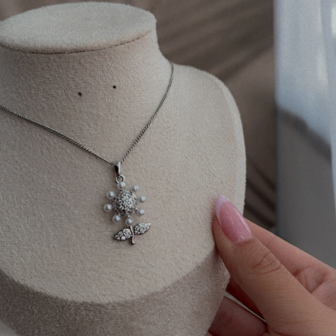 Cadena en rodio con dije de flor de perlas sobre un busto de exhibición